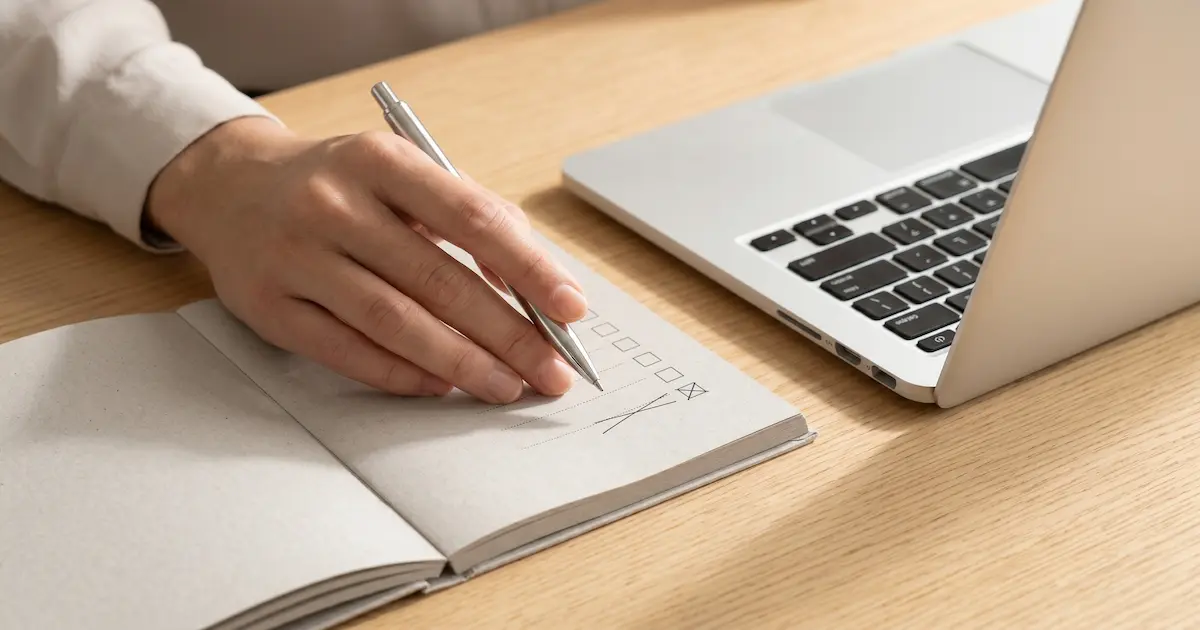 노트북 옆 플래너에 펜으로 체크하는 모습